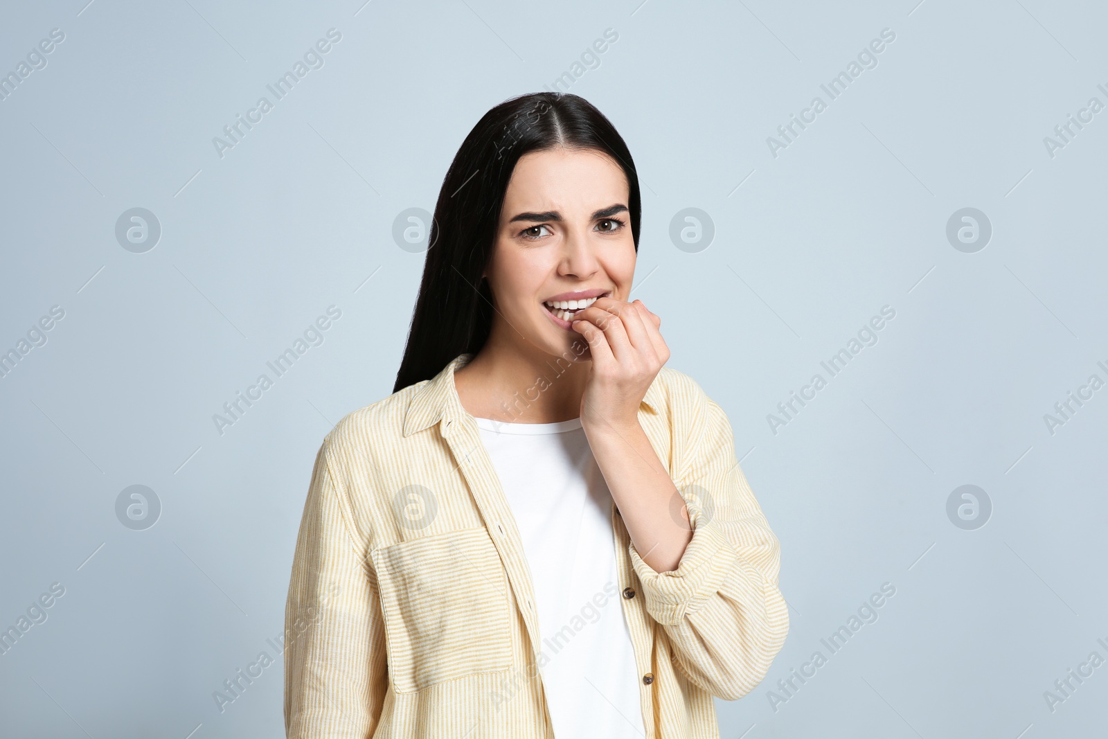 Photo of Young woman biting her nails on light grey background