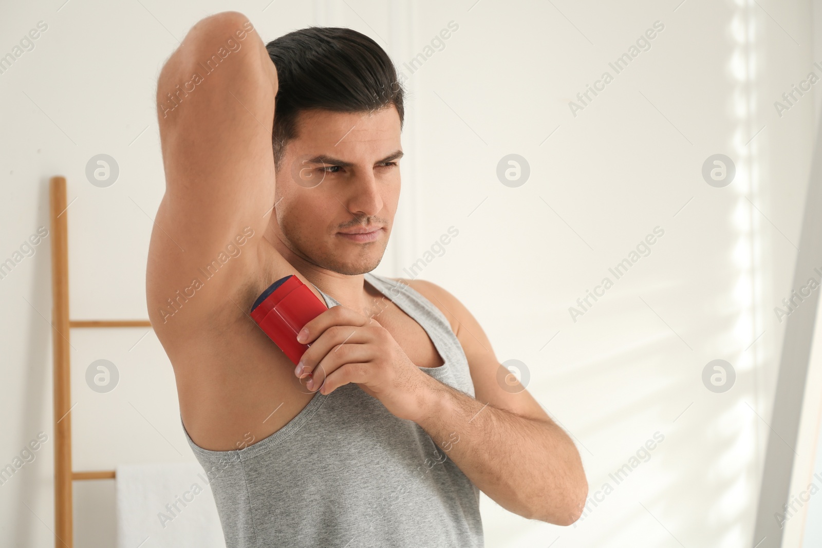 Photo of Handsome man applying deodorant to armpit at home, space for text