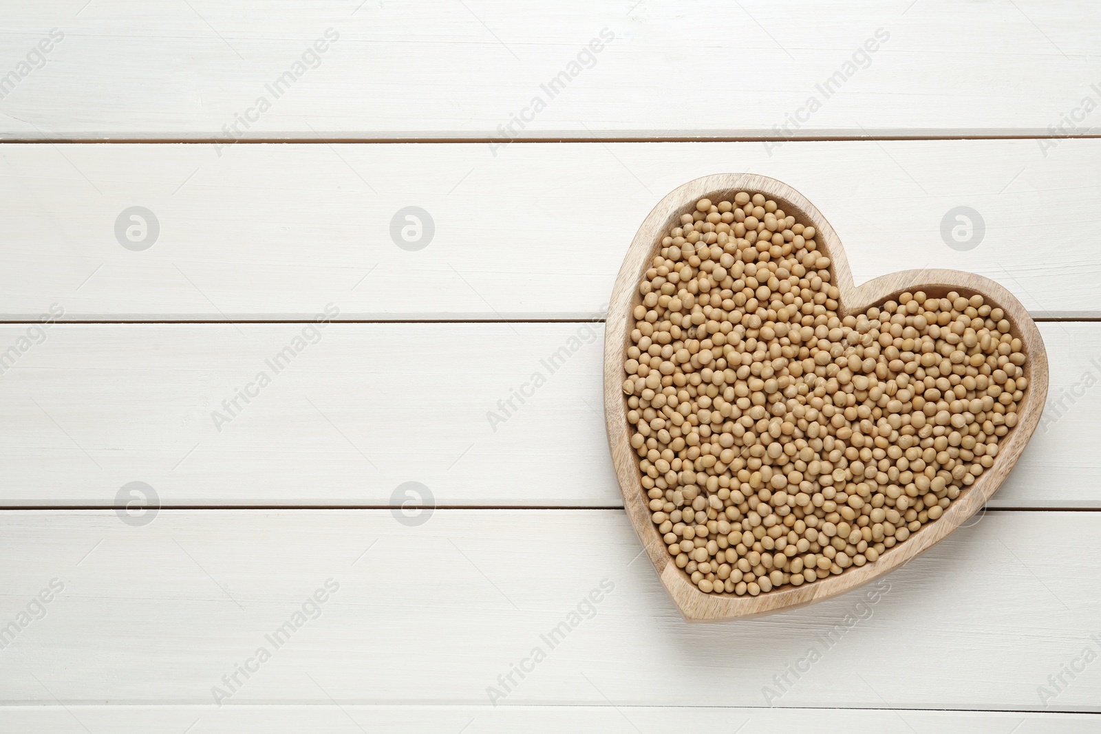 Photo of Soy in heart shaped bowl on white wooden table, top view. Space for text