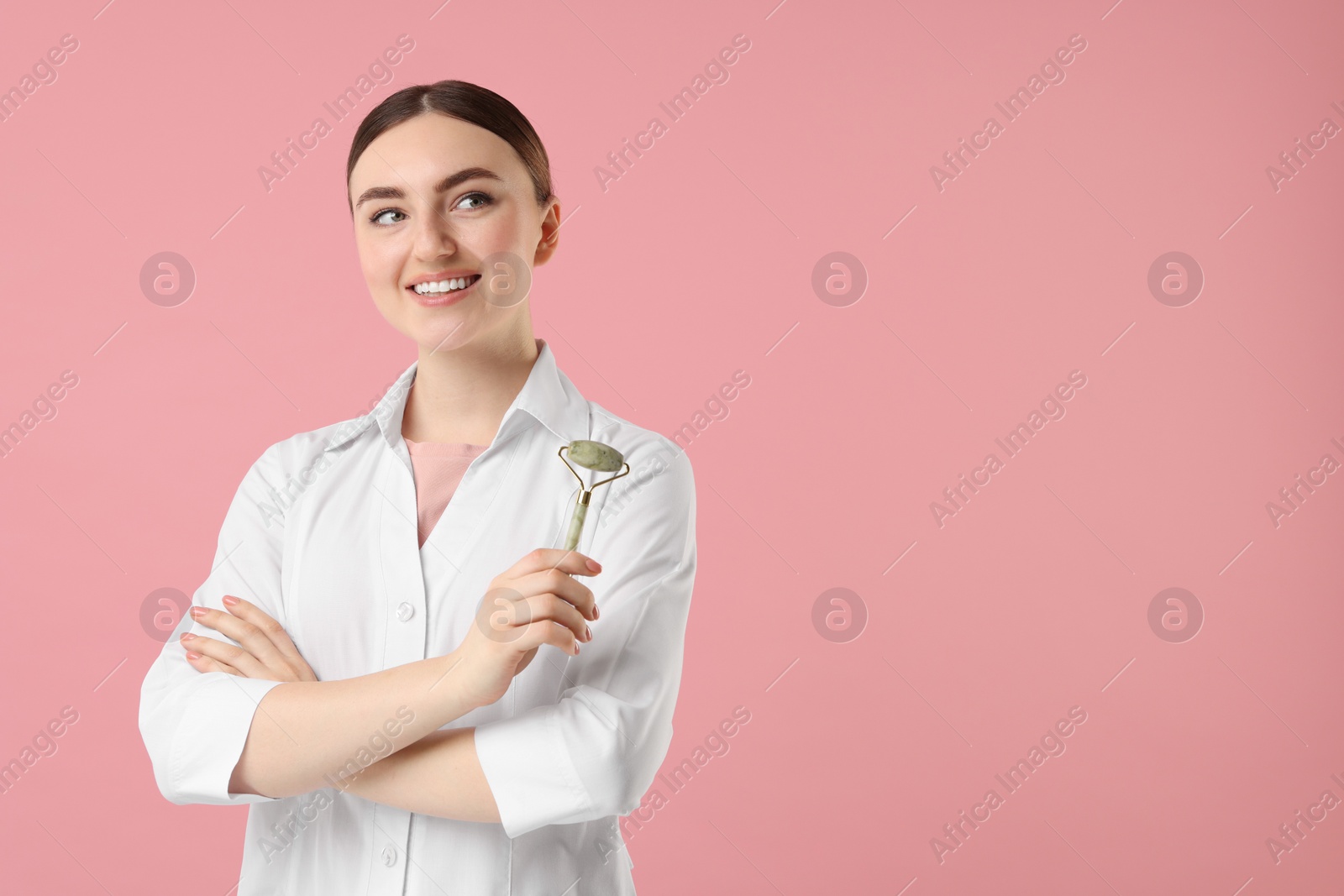 Photo of Cosmetologist with facial roller on pink background, space for text