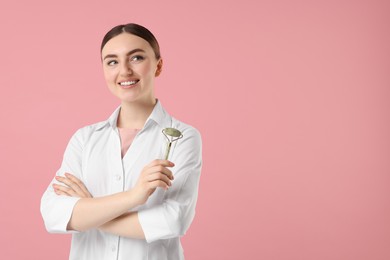 Photo of Cosmetologist with facial roller on pink background, space for text