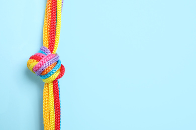 Photo of Top view of colorful ropes tied together on light blue background, space for text. Unity concept