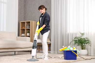 Photo of Young housewife vacuuming carpet at home. Cleaning chores