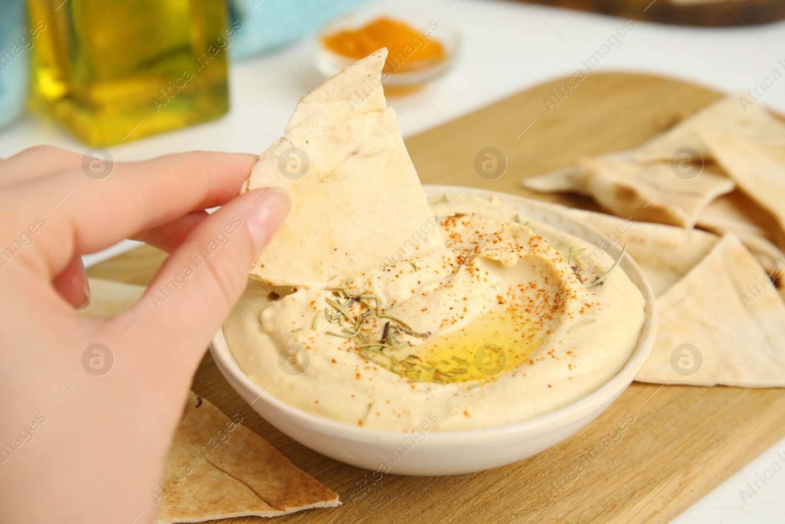 Photo of Woman dipping pita chip into hummus at table, closeup