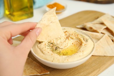 Photo of Woman dipping pita chip into hummus at table, closeup