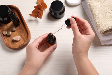 Photo of Woman with bottle of cosmetic serum and pipette at white wooden table, top view