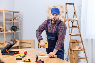 Young worker using electric drill at table in workshop