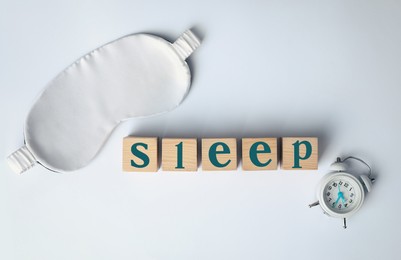 Photo of Word Sleep made of wooden cubes near blindfold and alarm clock on white background, flat lay. Insomnia treatment