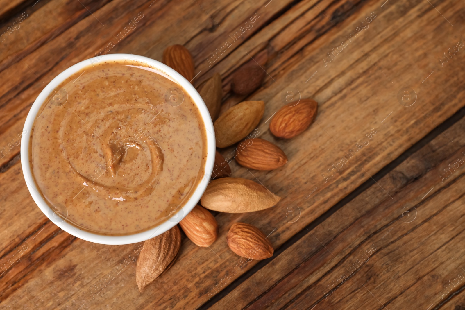 Photo of Delicious nut butter in bowl and almonds on wooden table, top view. Space for text