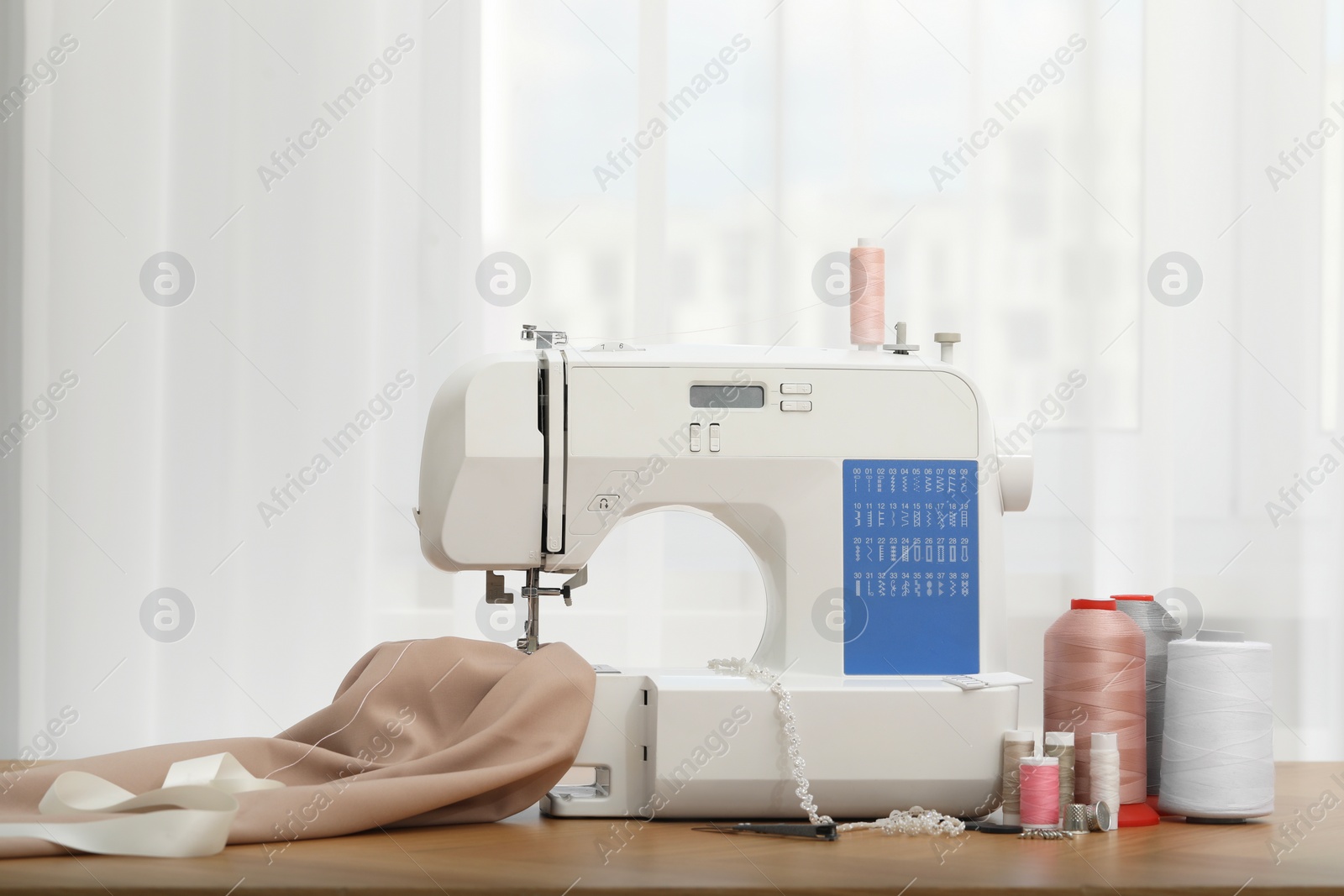 Photo of Sewing machine with fabric and craft accessories on wooden table indoors