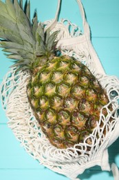 Photo of Whole ripe pineapple in mesh bag on light blue wooden table, top view