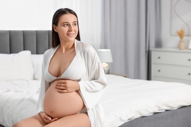 Photo of Beautiful pregnant woman in stylish comfortable underwear and robe on bed at home, space for text