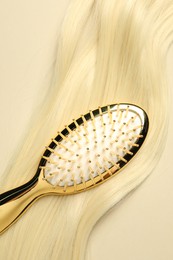 Photo of Stylish brush with blonde hair strand on beige background, top view