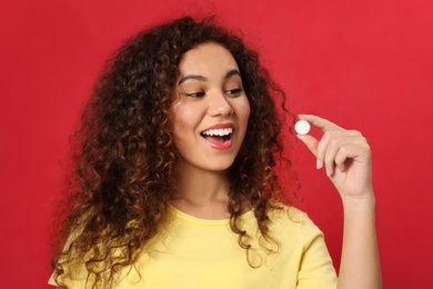 Photo of Emotional African-American woman with vitamin pill on red background
