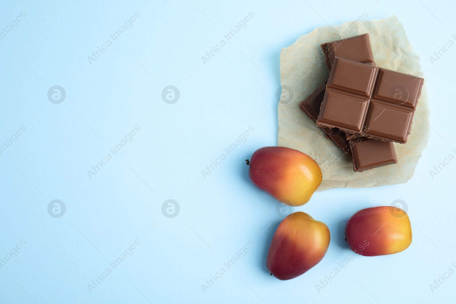Image of Fresh ripe palm oil fruits and chocolates on light blue background, flat lay. Space for text