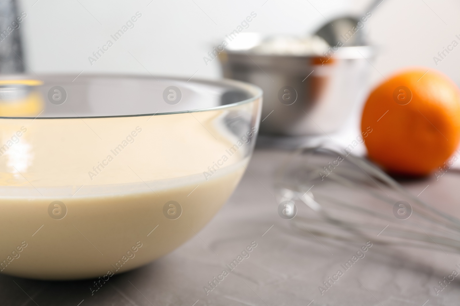 Photo of Glass bowl with batter on grey table, closeup. Space for text