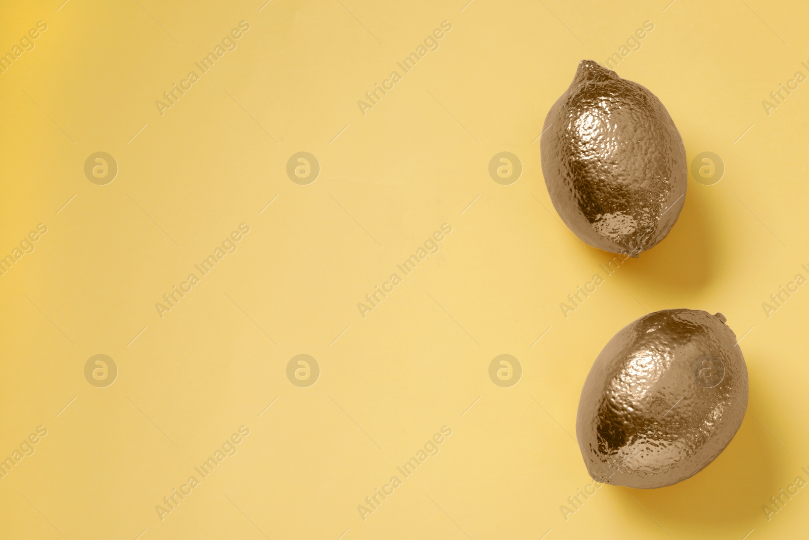 Photo of Golden lemons on yellow background, flat lay. Space for text