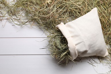 Photo of Burlap sack with dried hay on white wooden table, top view. Space for text