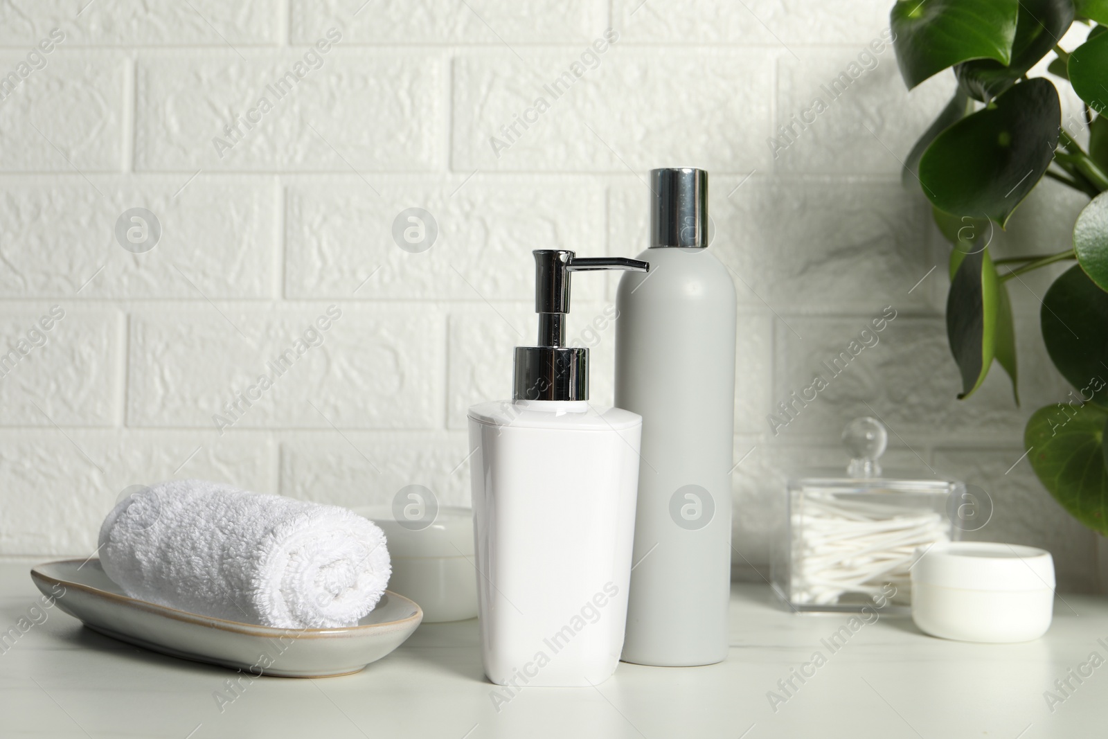 Photo of Different bath accessories and personal care products on white table near brick wall