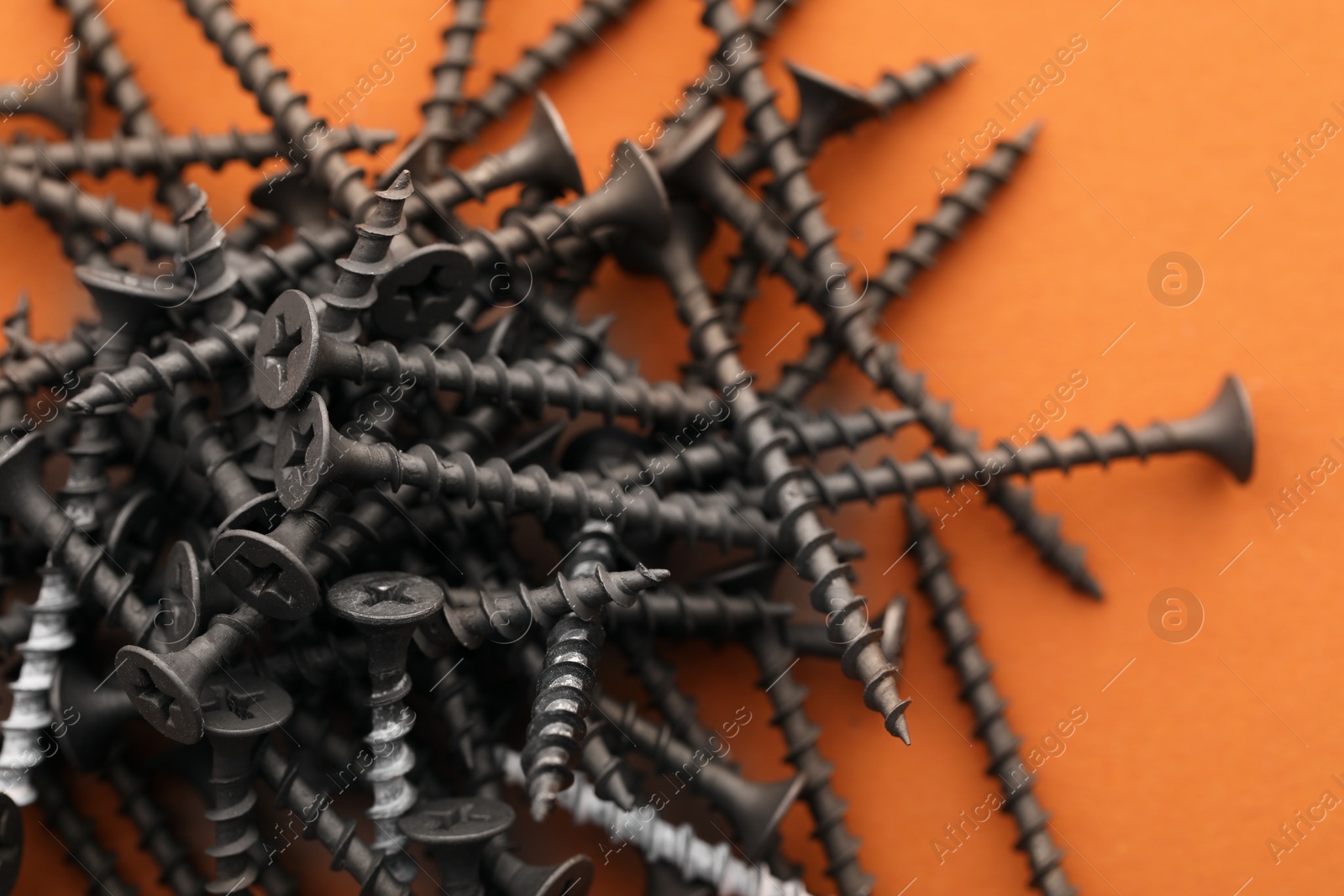 Photo of Many metal screws on orange background, closeup