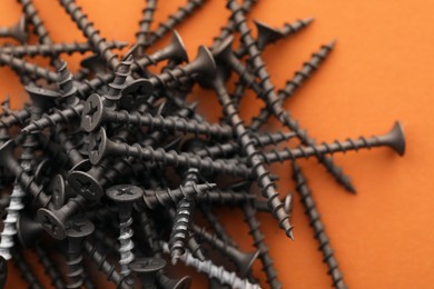 Photo of Many metal screws on orange background, closeup