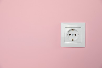 Power socket on pink wall, space for text. Electrical supply