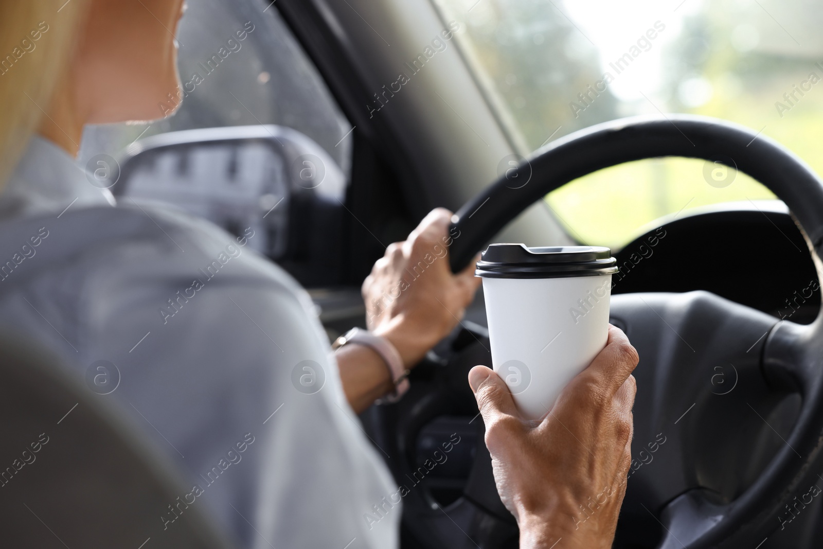 Photo of Coffee to go. Woman with paper cup of drink driving her car, closeup