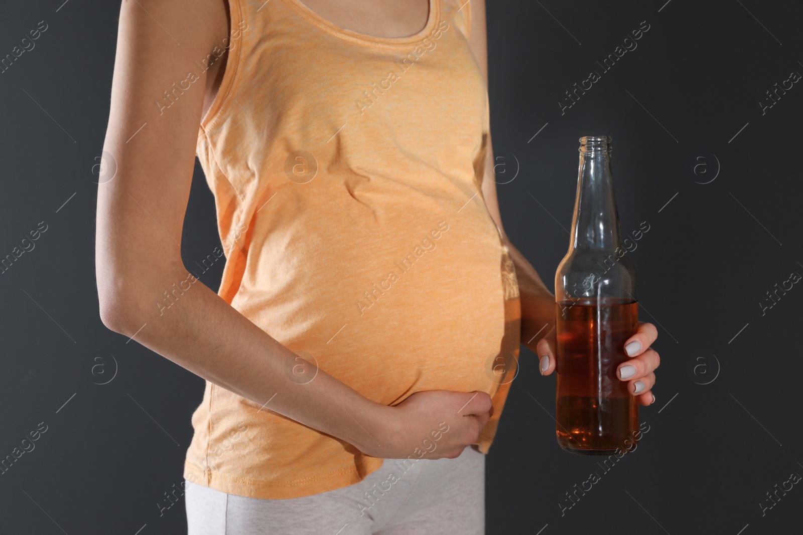 Photo of Future mother with bottle of alcohol drink on black background, closeup. Bad habits during pregnancy