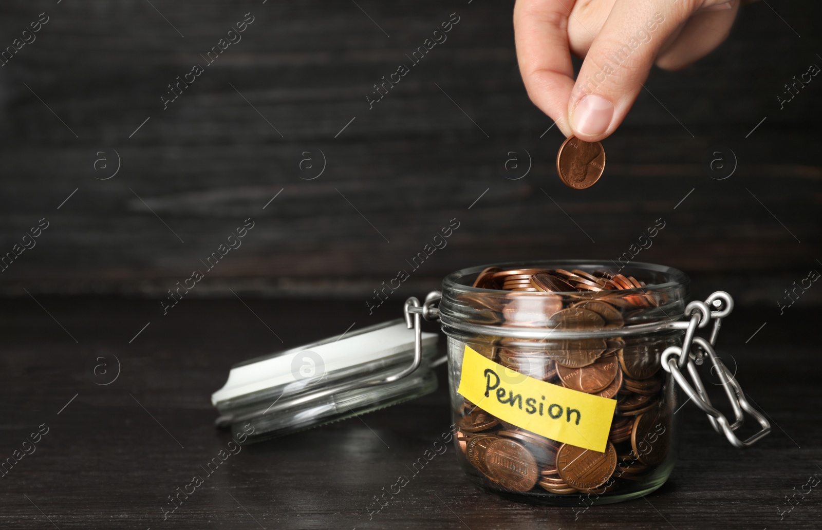 Photo of Woman putting coin in glass jar with label "PENSION" on table, closeup. Space for text