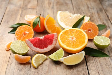 Photo of Different citrus fruits with fresh leaves on wooden table