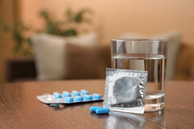 Photo of Glass of water, condom and pills on wooden table indoors, space for text. Potency problem concept