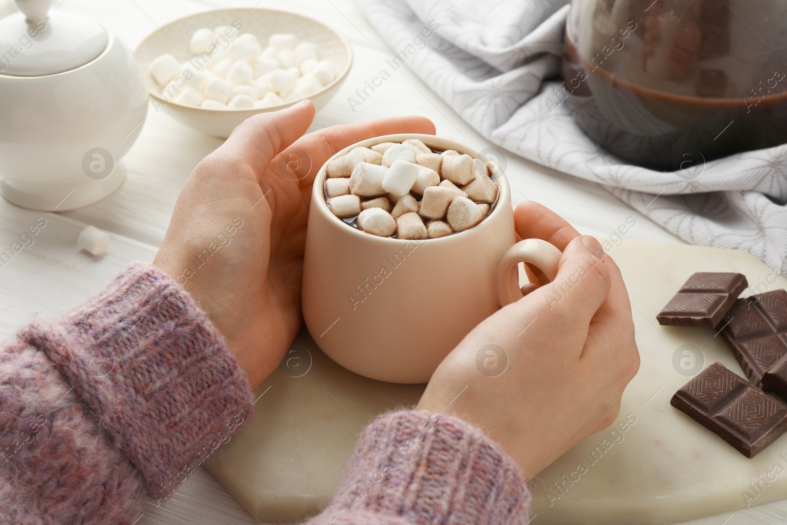 Photo of Woman holding cup of aromatic hot chocolate with marshmallows at table, closeup