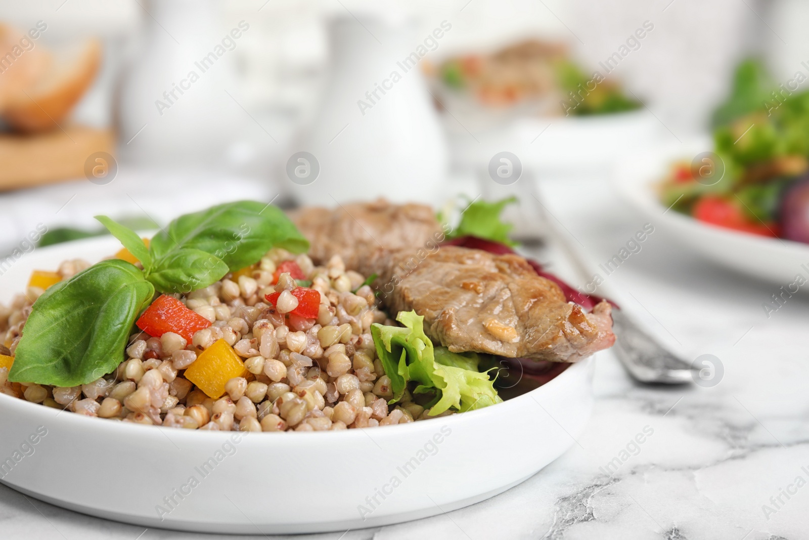 Photo of Tasty buckwheat porridge with meat on white marble table