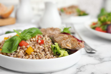 Photo of Tasty buckwheat porridge with meat on white marble table