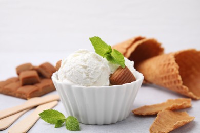 Scoops of tasty ice cream with mint leaves and caramel candies on white table, closeup