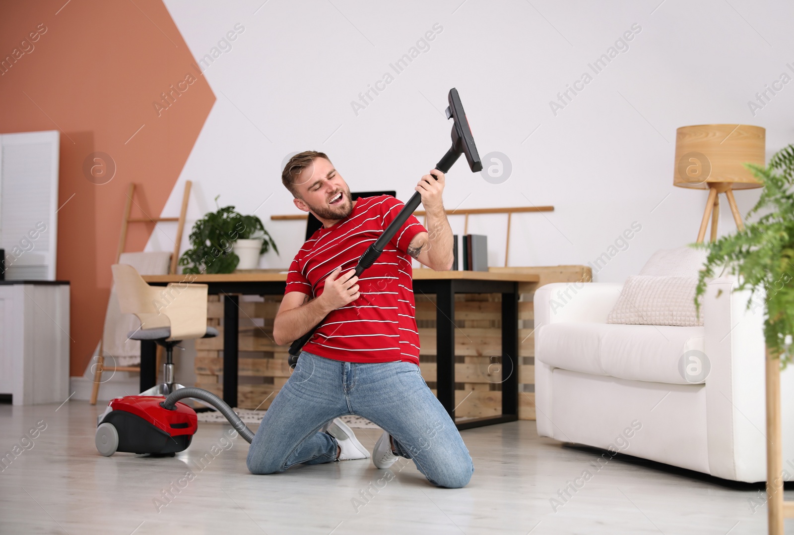 Photo of Young man having fun while vacuuming at home