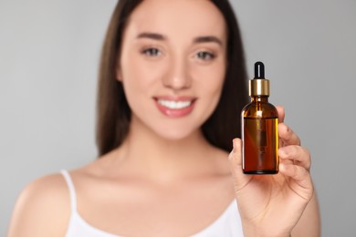 Woman with essential oil on light grey background, selective focus. Space for text