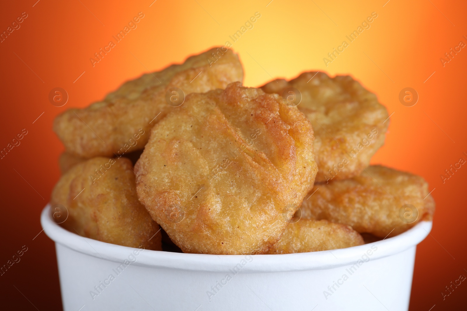 Photo of Bucket with delicious chicken nuggets on orange background, closeup