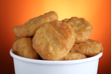 Photo of Bucket with delicious chicken nuggets on orange background, closeup