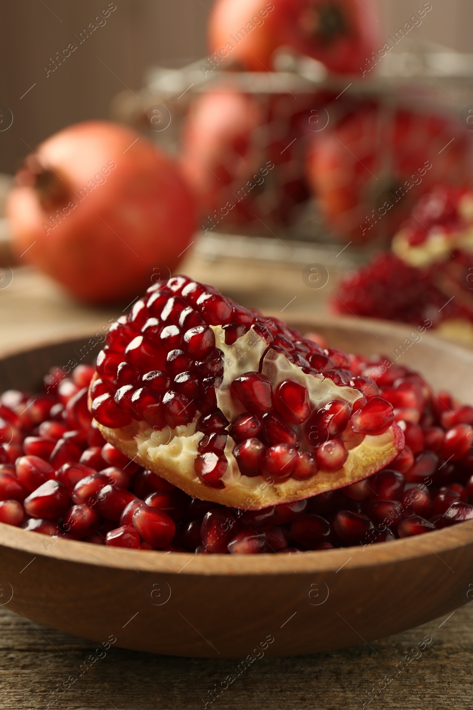 Photo of Ripe juicy pomegranate grains in bowl on wooden table, closeup