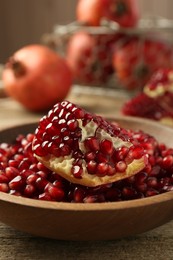 Photo of Ripe juicy pomegranate grains in bowl on wooden table, closeup