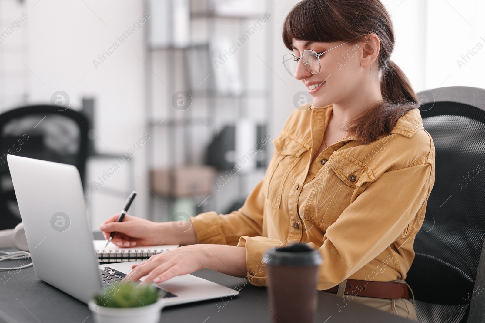 Photo of Woman taking notes during webinar at table indoors