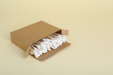 Box with wooden cotton buds on beige background. Space for text