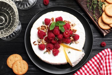 Photo of Brie cheese served with raspberries and walnuts on black wooden table, flat lay