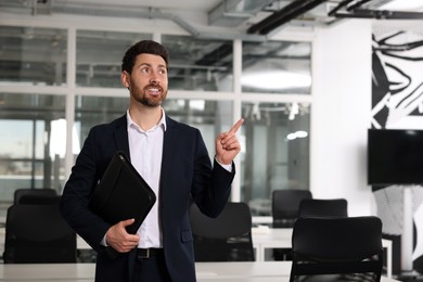 Photo of Happy real estate agent with leather portfolio pointing indoors