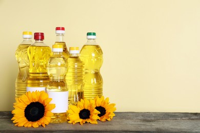 Bottles of cooking oil and sunflowers on wooden table, space for text