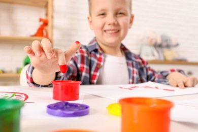 Photo of Little boy painting with finger at white table indoors, focus on hand