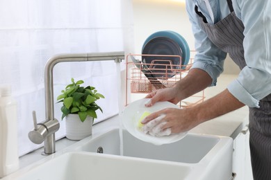 Photo of Man washing plate above sink in kitchen, closeup