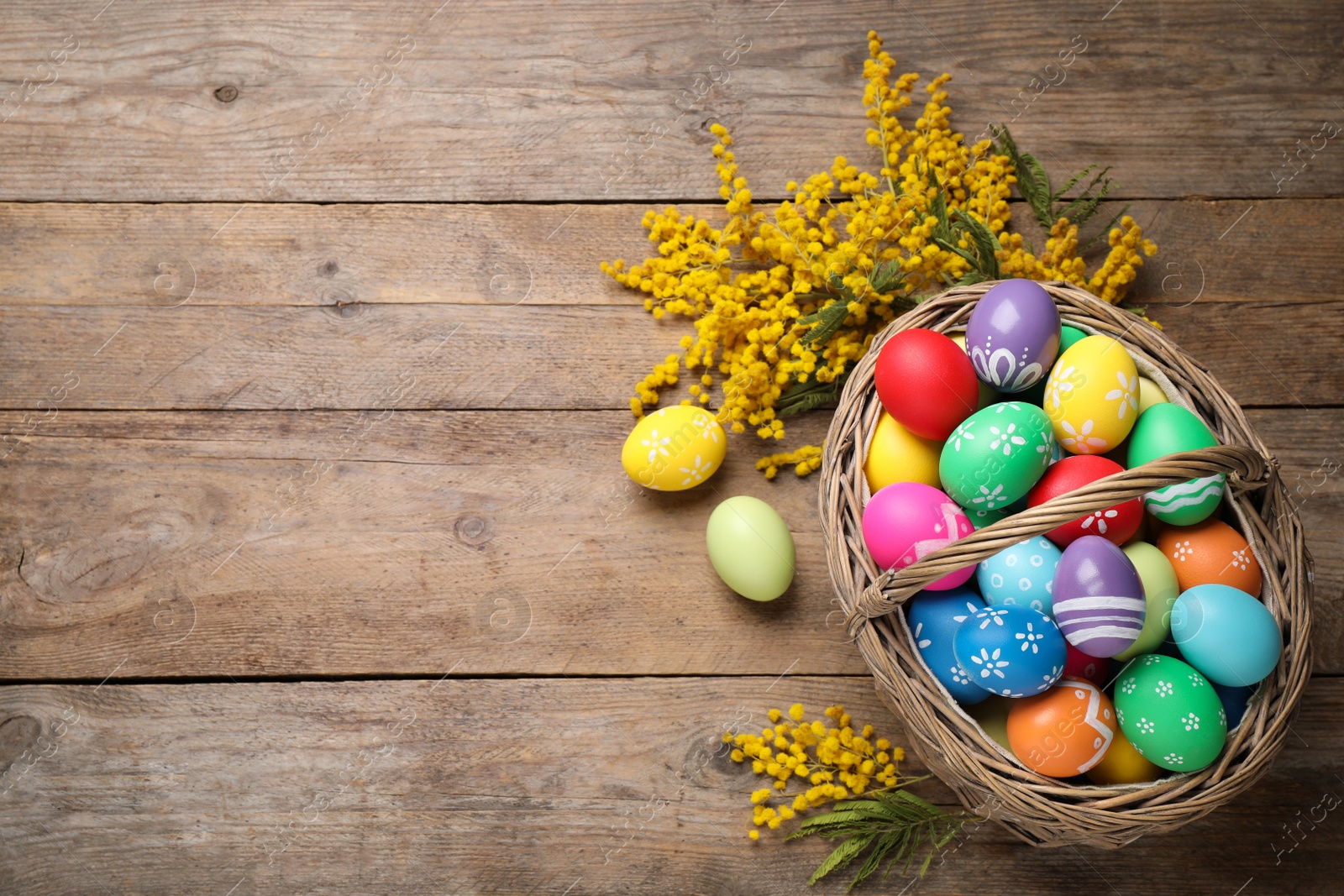 Photo of Colorful Easter eggs and mimosa flowers on wooden background, flat lay. Space for text