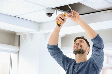 Technician installing CCTV camera on ceiling indoors